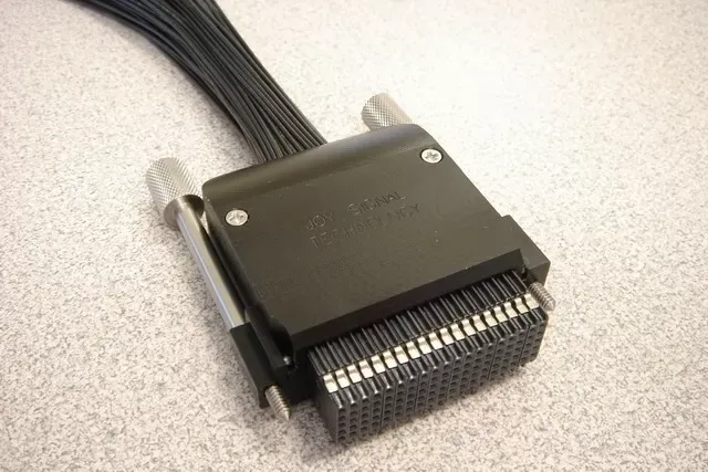 A black SCSI connector with a multi-wire cable extending upward, resting on a speckled surface.