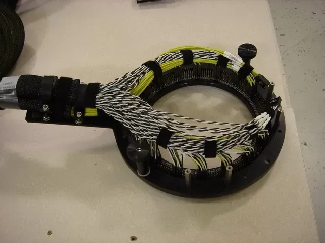 A circular ring mounting component connected to a thick, multi-colored bundle of wires secured by black Velcro straps.