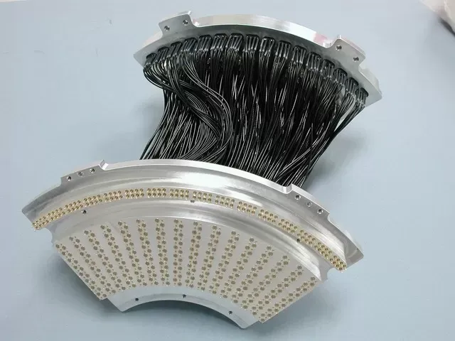 Two metal, semi-circular housings connected by a dense bundle of black cables, with many small, gold-tipped connectors.