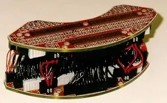 A curved red circuit board stack with black and white connectors joined by short red and black wires.