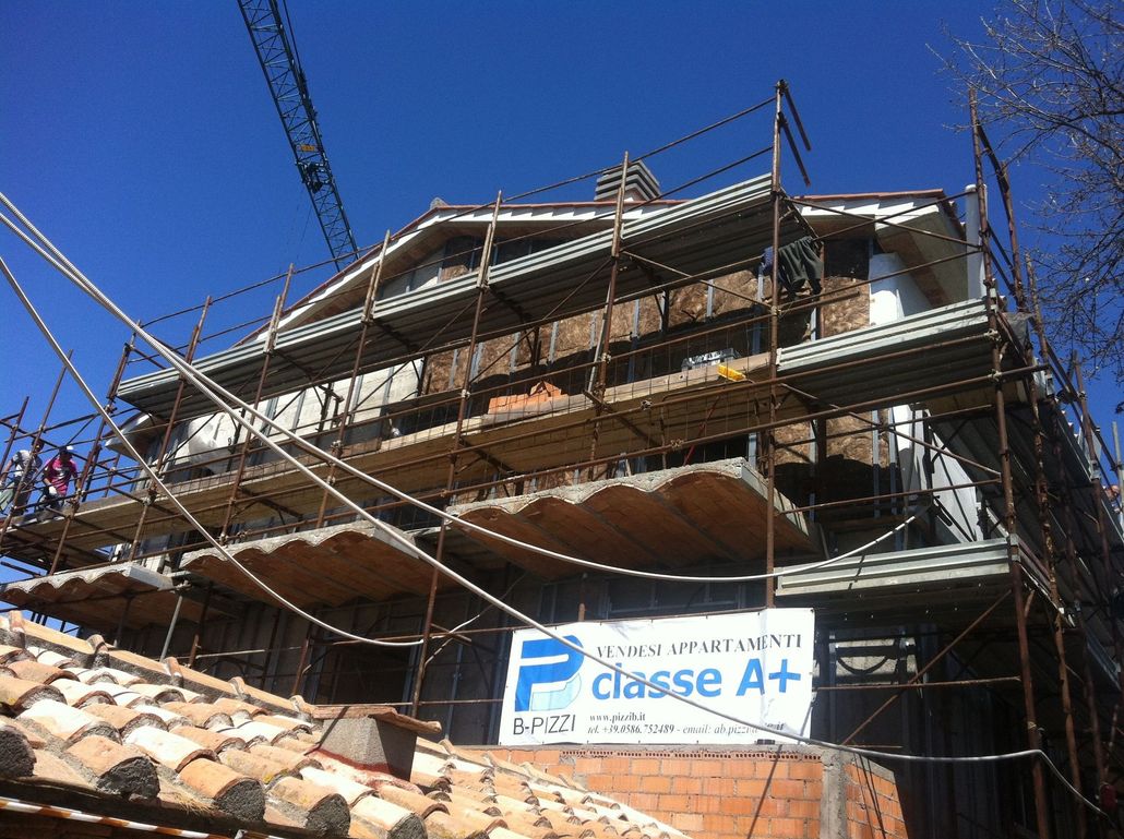 Casa in costruzione con impalcature e un'insegna "Classe A+" contro un cielo azzurro.
