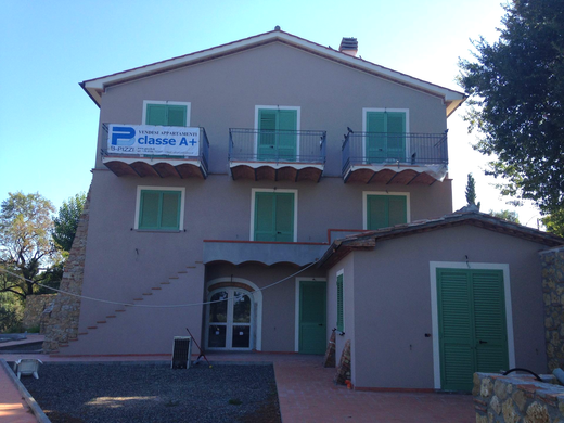 Casa a un solo piano color crema con persiane verdi e tetto di tegole rosse, adiacente a un vialetto pavimentato.