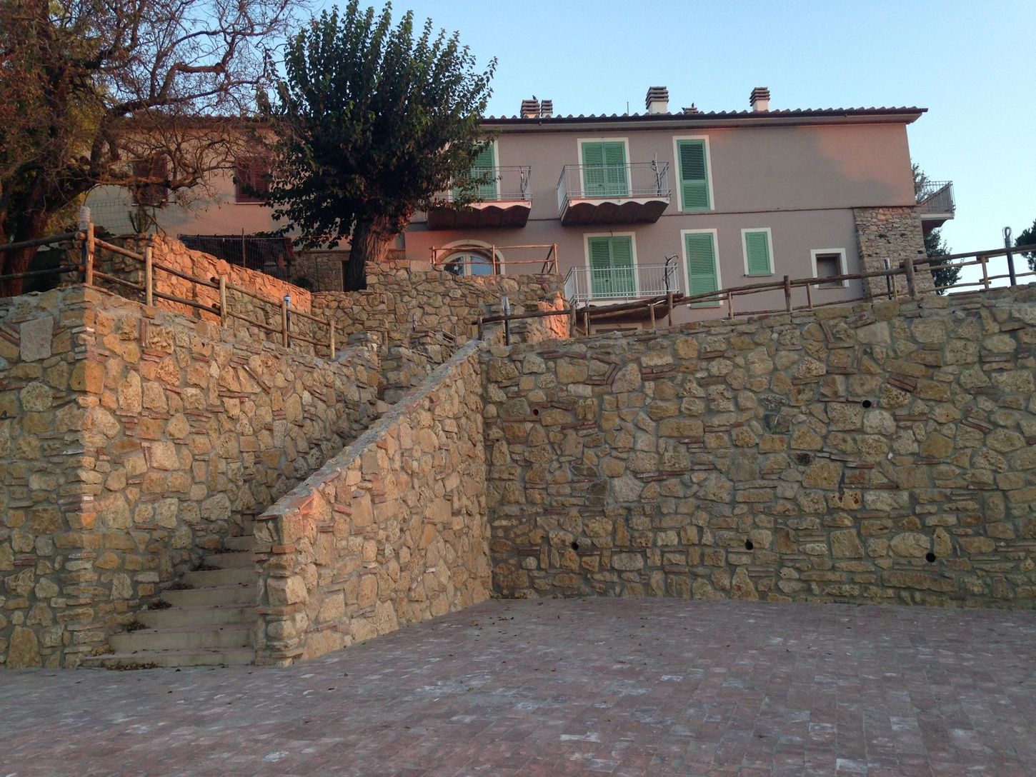 Una scalinata in pietra conduce a una casa rosa con persiane verdi su un muro di cinta.