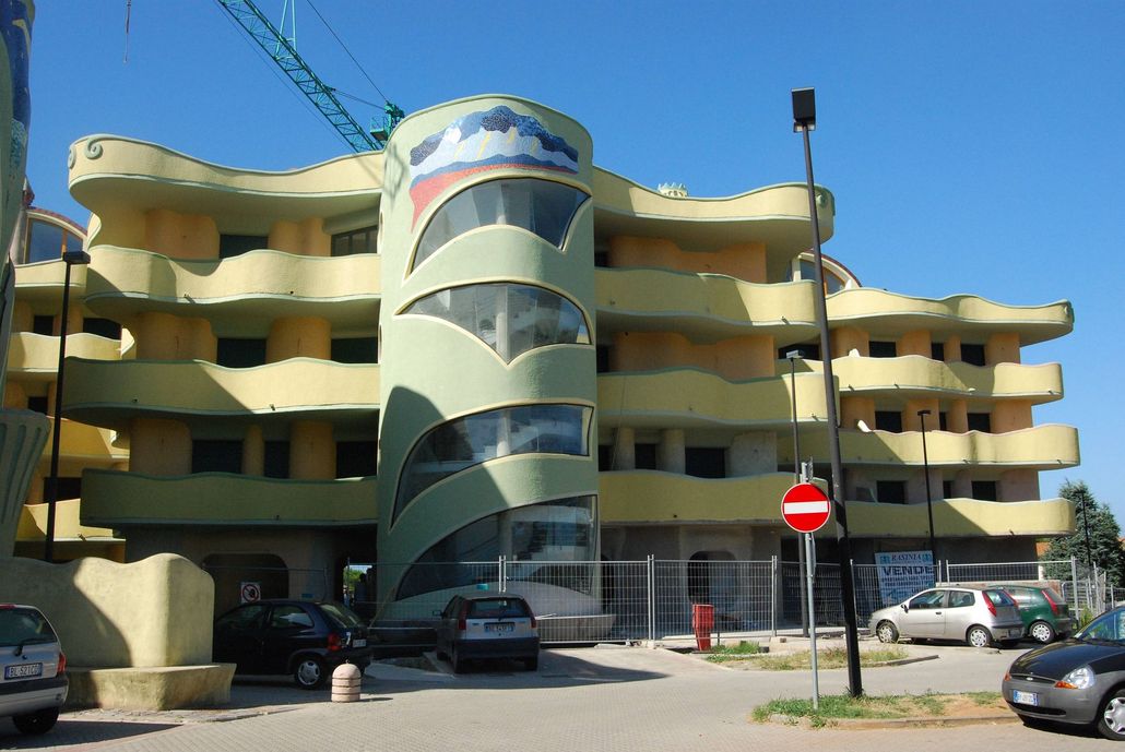 Palazzo residenziale con balconi curvi e auto parcheggiate sotto un cielo azzurro limpido.