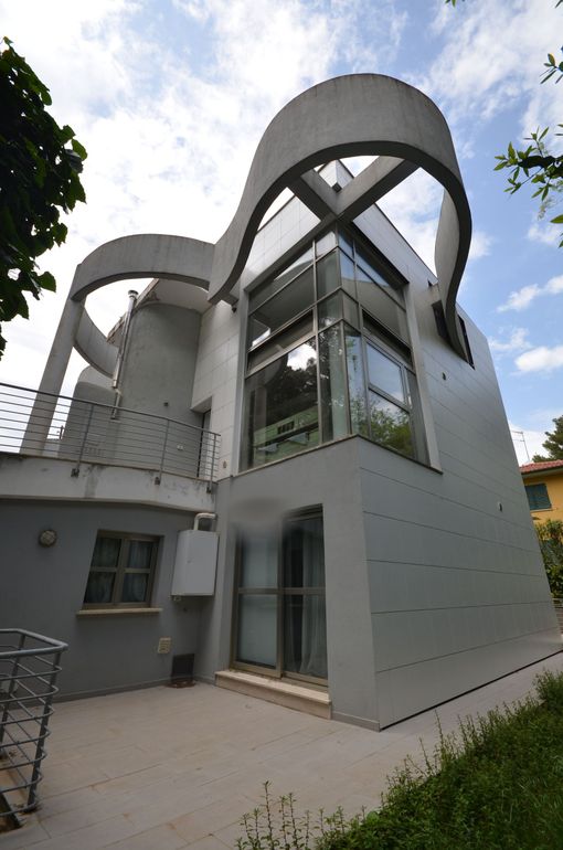 Moderno edificio grigio con tetto curvo e facciata in vetro, visto da un cortile.