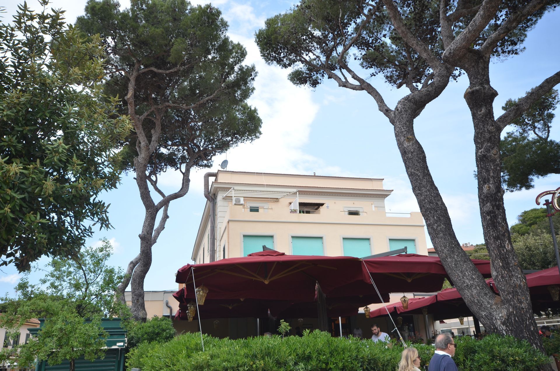 Tendalino rosso da caffè sotto alti pini di fronte a un edificio chiaro