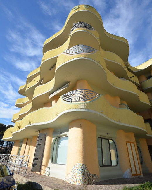 Palazzo residenziale giallo ondulato con balconi curvi contro un cielo blu