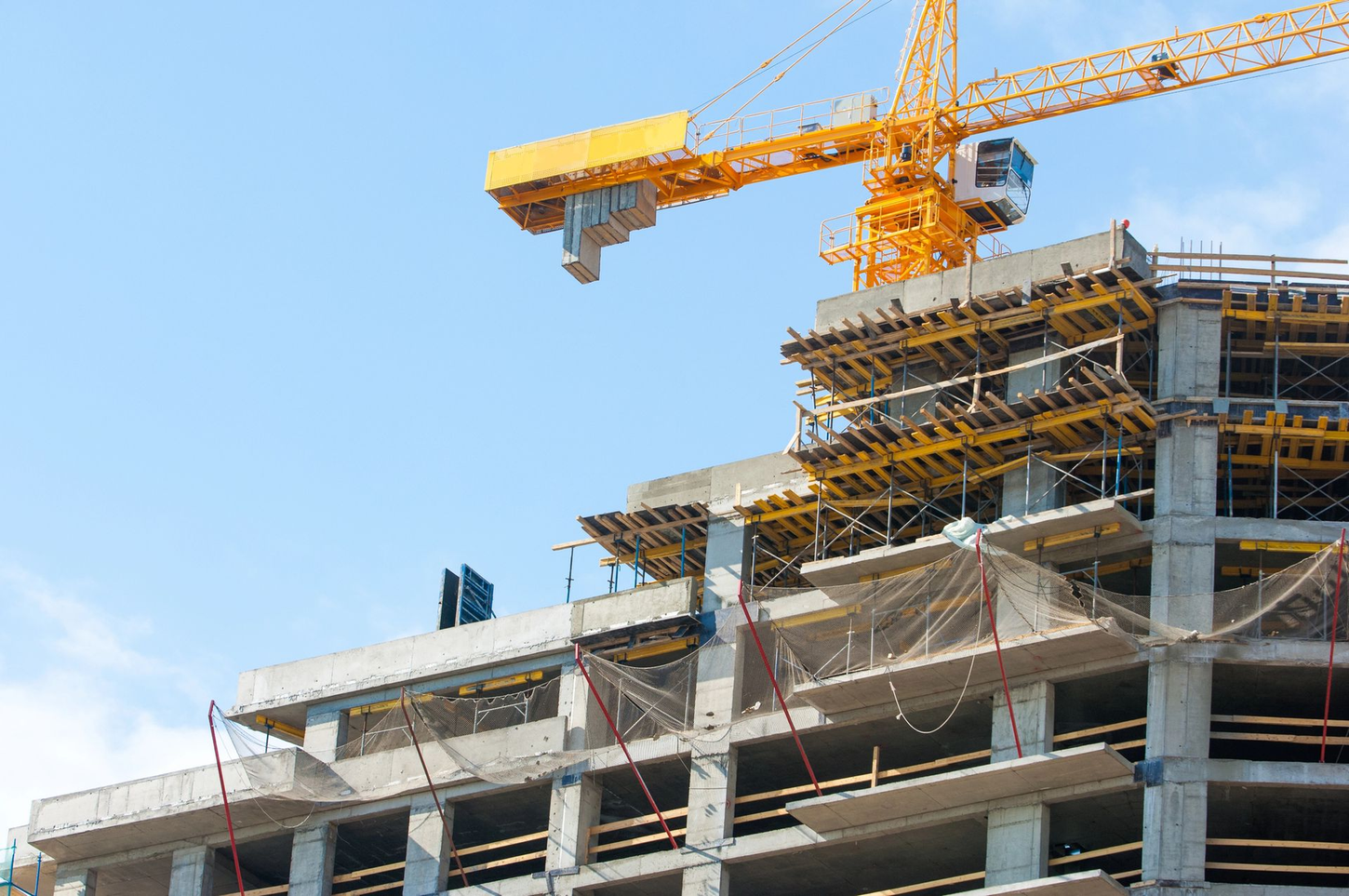 Cantiere edile con la struttura di un grattacielo e una gru a torre gialla sullo sfondo di un cielo azzurro.