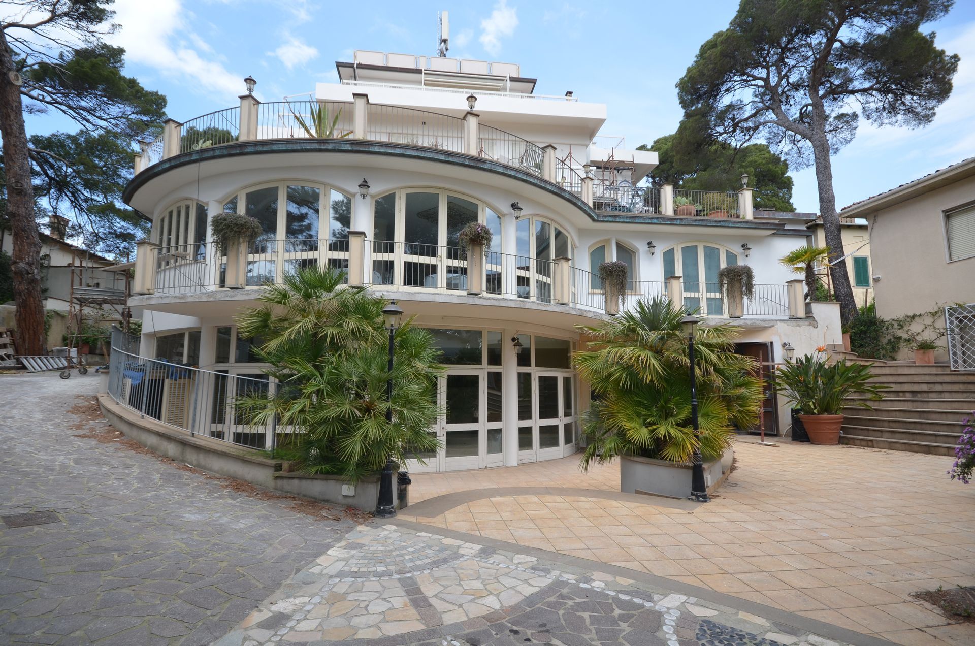 Grande casa bianca e rotonda con finestre di vetro curve, vialetto in pietra e alberi sotto un cielo azzurro