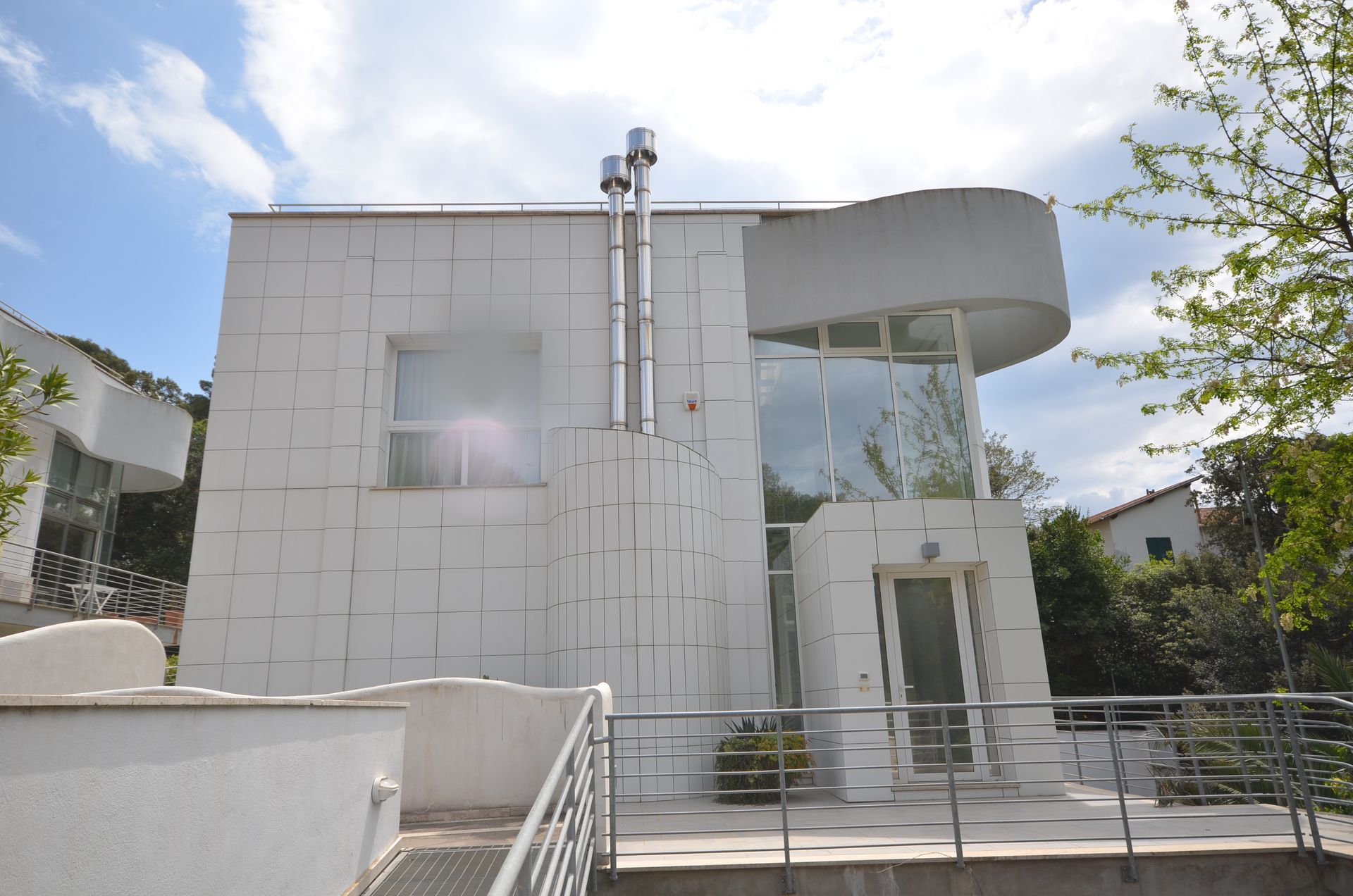 Casa moderna bianca a due piani con balcone curvo e grandi finestre sotto un cielo luminoso