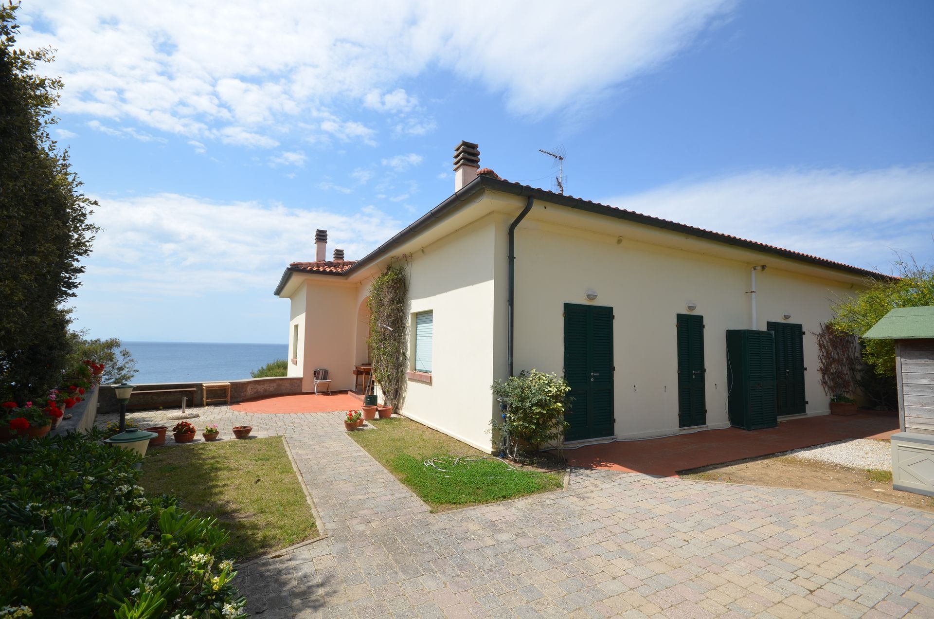 Casa di campagna bianca con persiane verdi, un vialetto rosso e un cielo azzurro brillante.