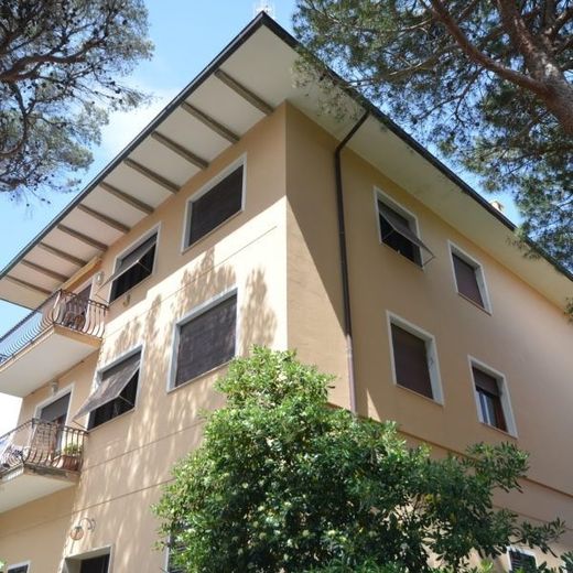 Palazzo di appartamenti beige con balconi e finestre, visto dal basso attraverso gli alberi.