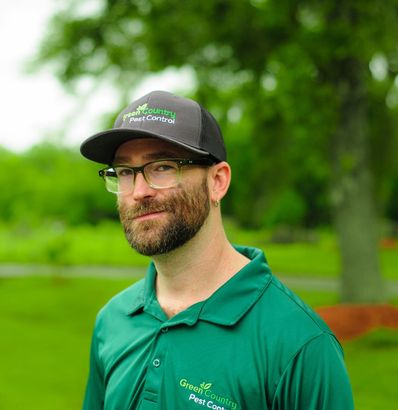Man in green shirt and hat, with beard and glasses, outdoors.