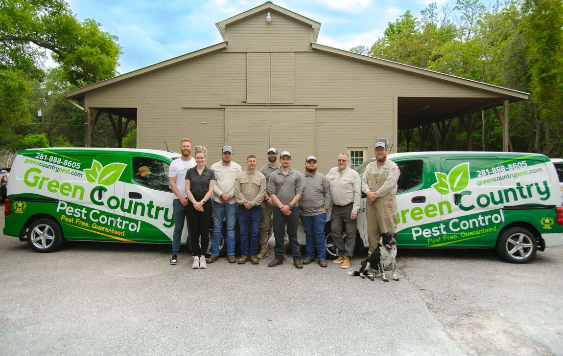 Green Country Pest Control team posing with vans in front of a tan building. Green and white vans are on either side.