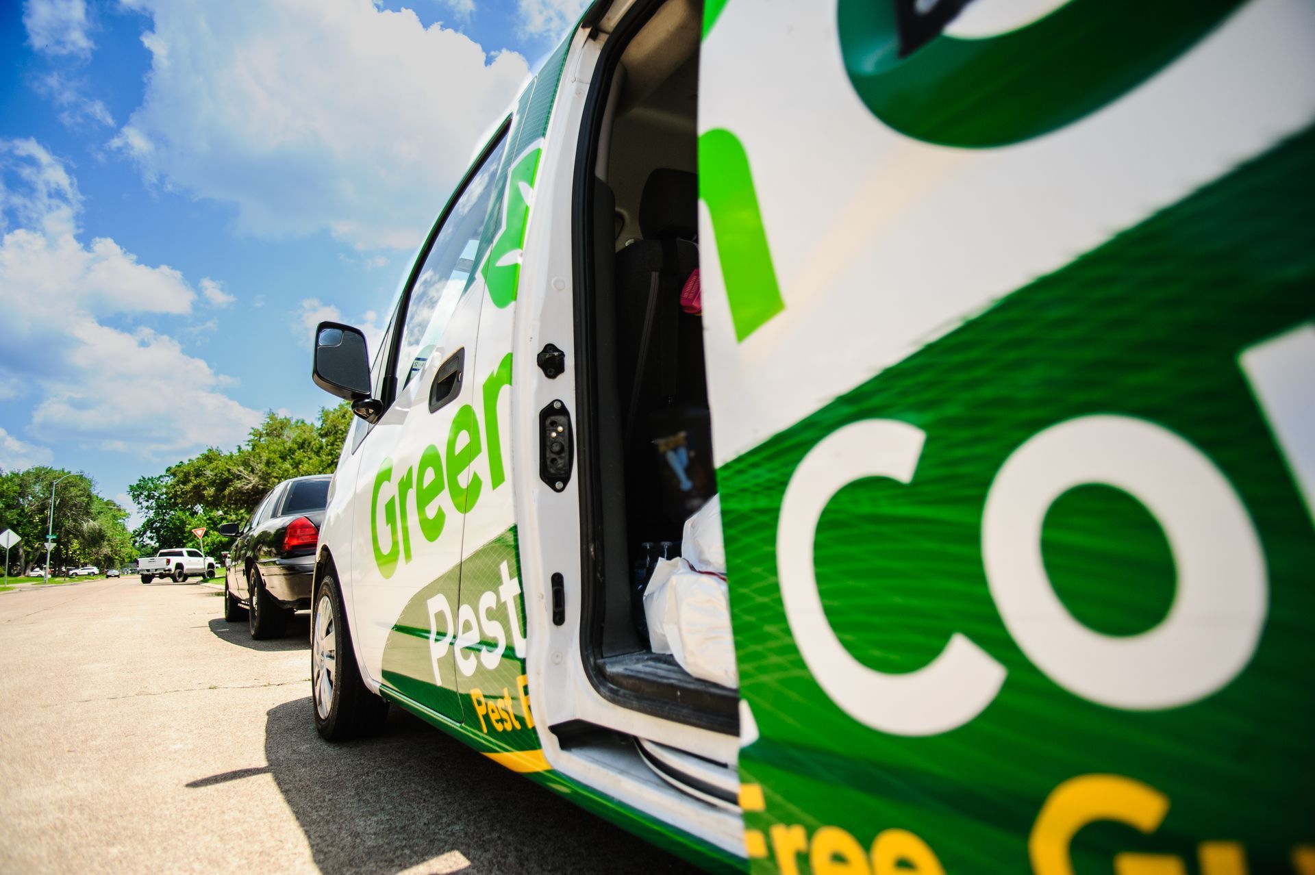 Green Pest Control van with open door parked on road under a blue sky.