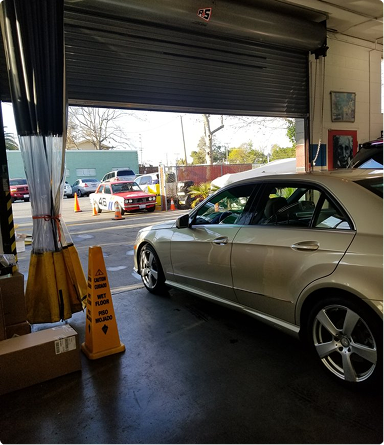 Silver sedan inside a garage with a partially open roll-up door, looking out to a street scene.  | Hudson Automotive