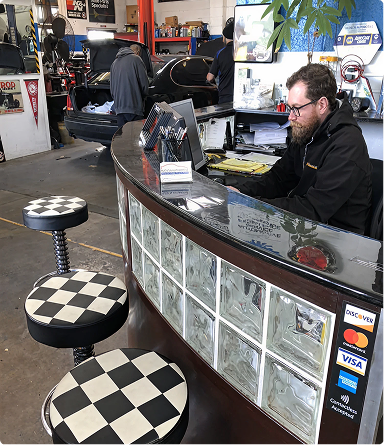 Man sitting at a diner counter with checkered stools and a glossy curved counter in a retro interior | Hudson Automotive