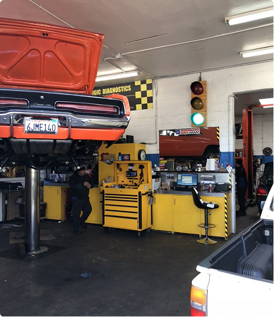 Classic car lifted in a garage with its hood open, near yellow tools and a traffic light display | Hudson Automotive