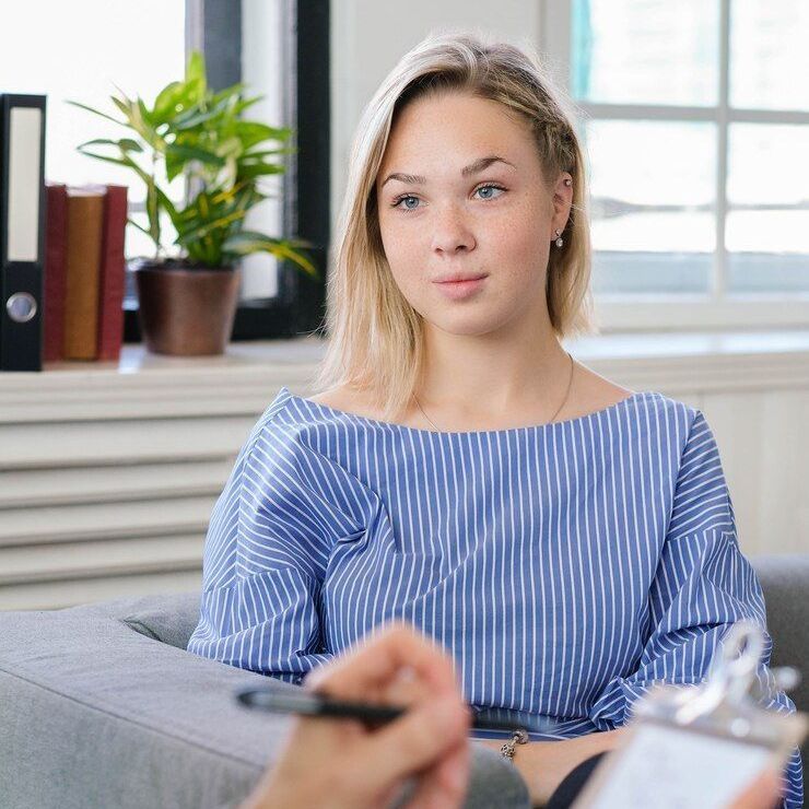A woman is sitting on a couch talking to a man with a clipboard.