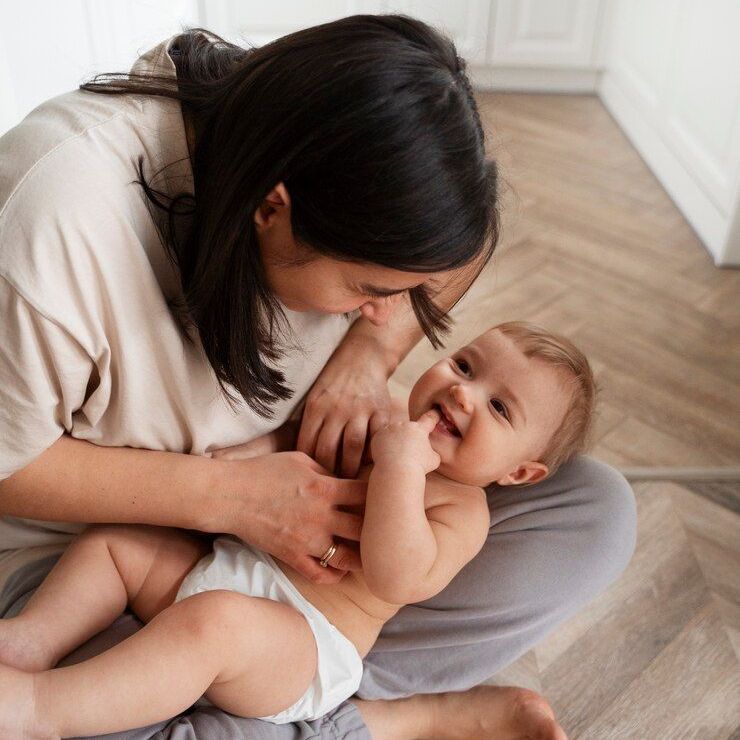 A woman is sitting on the floor holding a baby in a diaper.