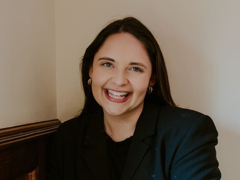 Morgan Wright in a black blazer sitting against a beige wall