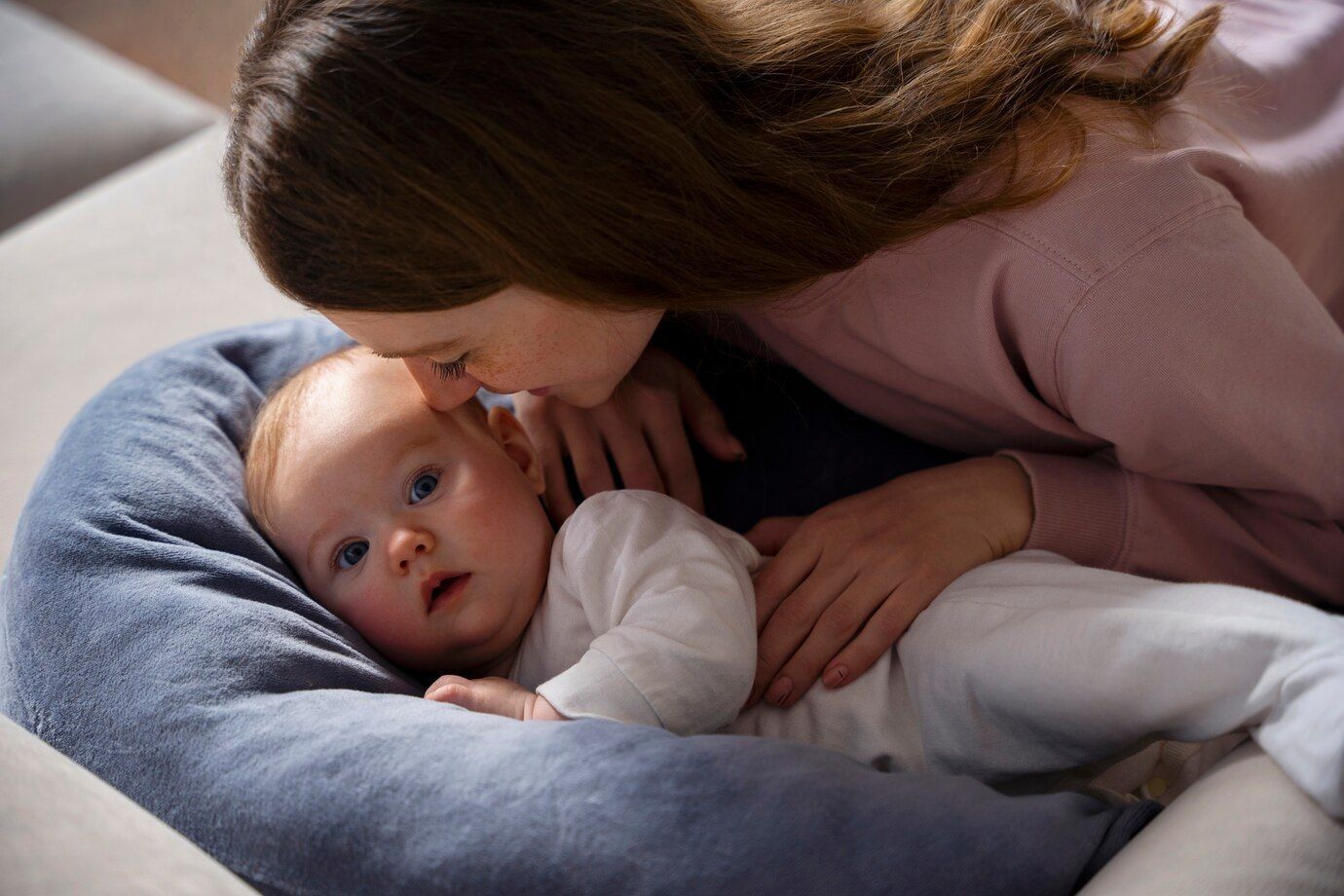 A woman is kissing a baby on the forehead while laying on a couch.