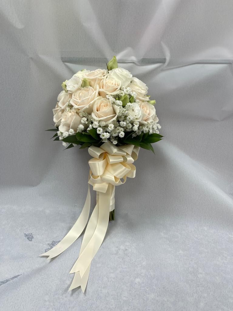Bouquet da sposa bianco con rose color crema, verde e lunghi nastri color avorio su sfondo grigio.