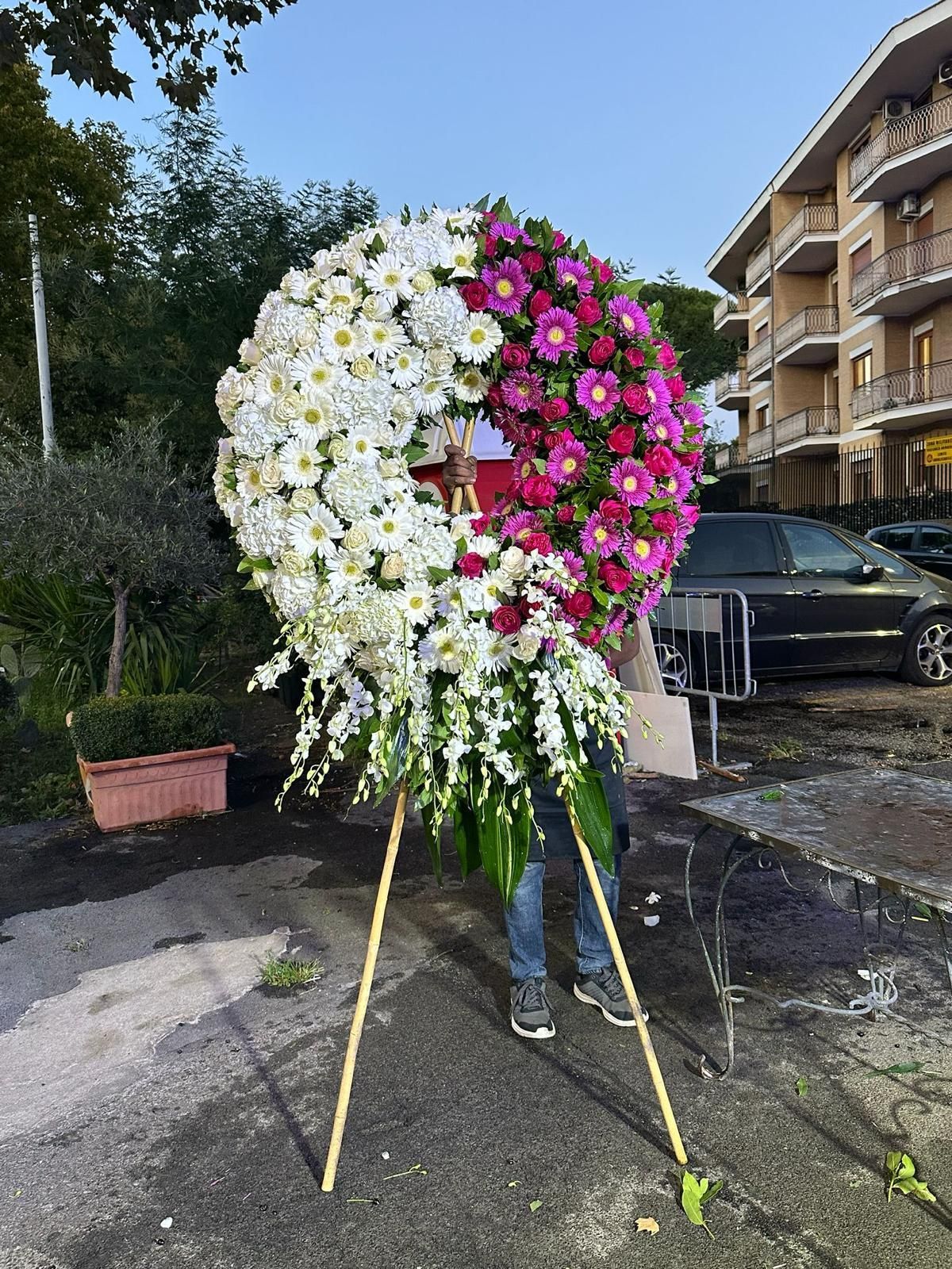 Grande ghirlanda floreale bianca e rosa su un treppiede all'aperto, accanto a un condominio.