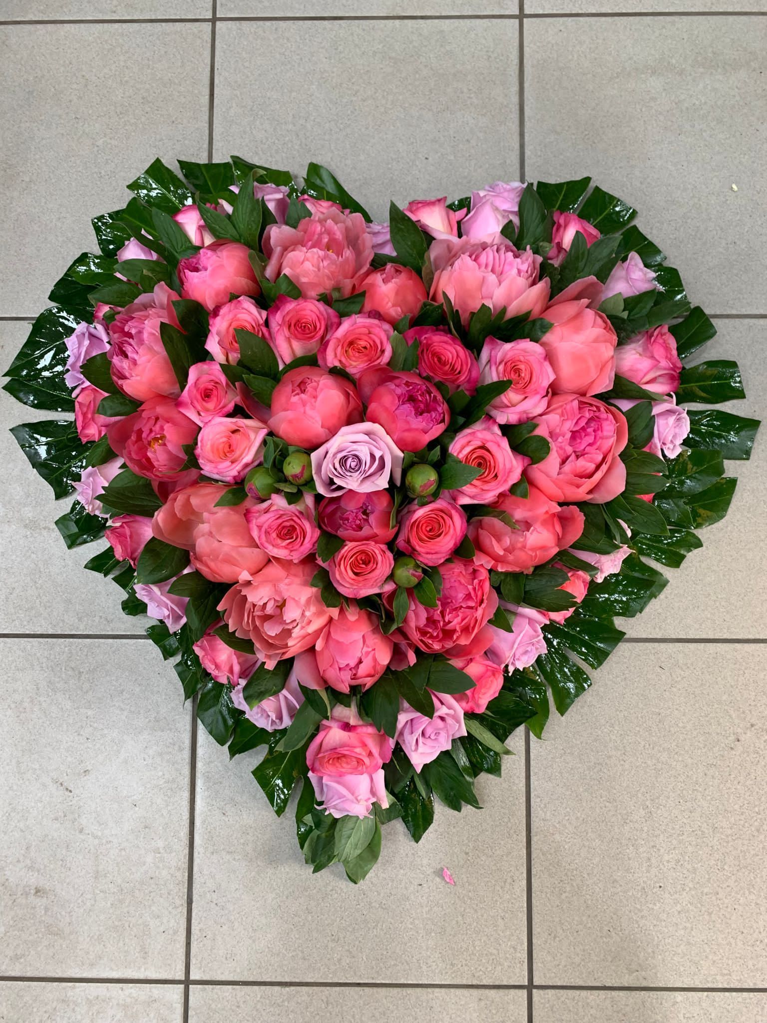 Bouquet di fiori rosa a forma di cuore con foglie verdi su un pavimento piastrellato grigio.