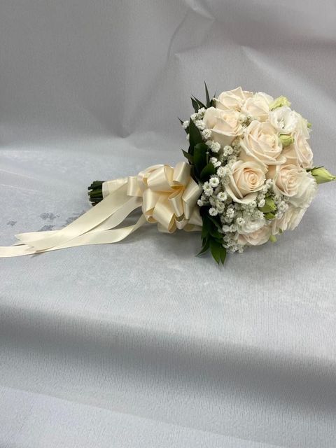 Bouquet da sposa con rose bianche, nastro avorio e verde su sfondo grigio chiaro.