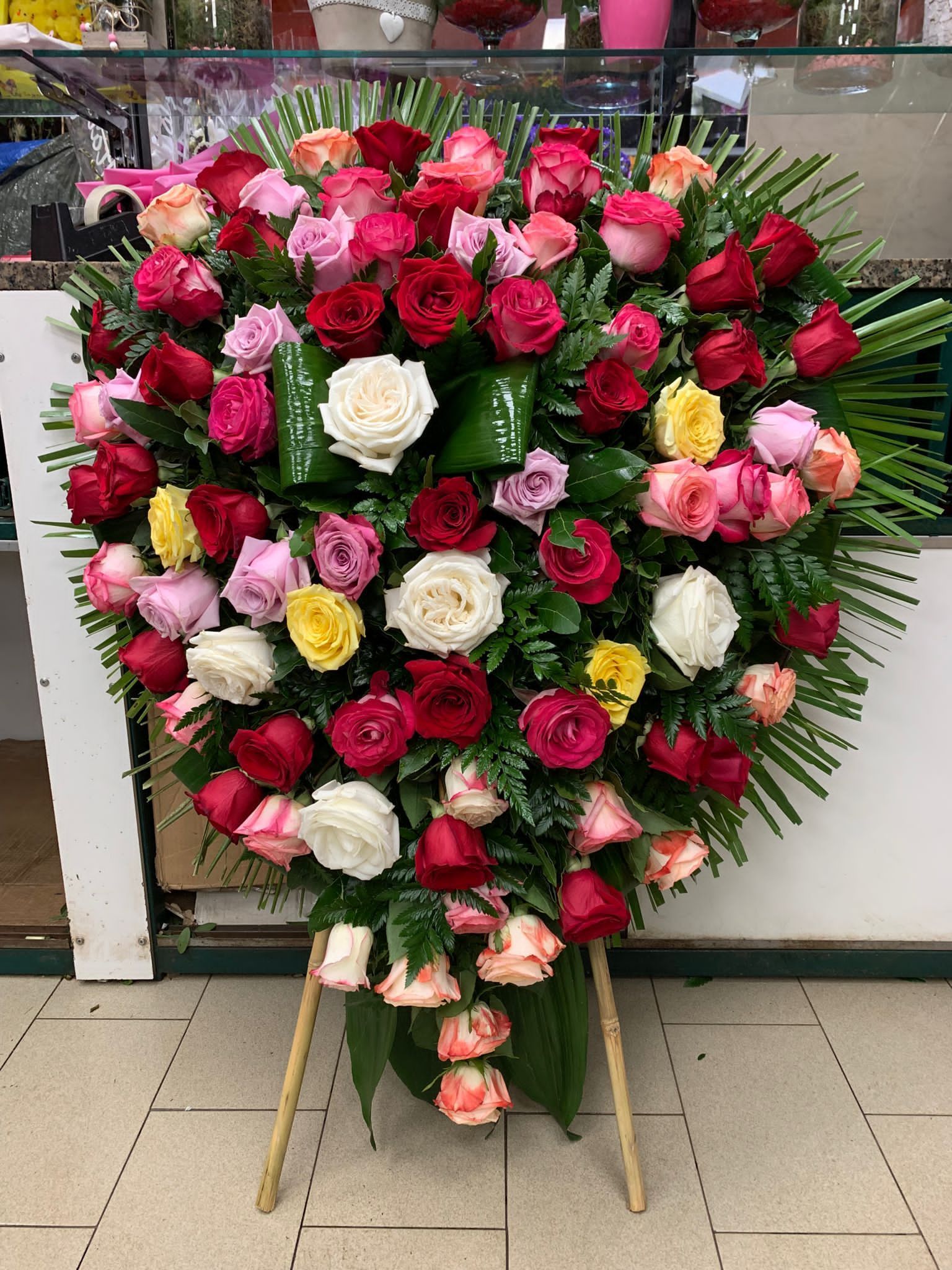 Bouquet a forma di cuore di rose rosa, rosse, bianche e gialle su un cavalletto all'aperto.