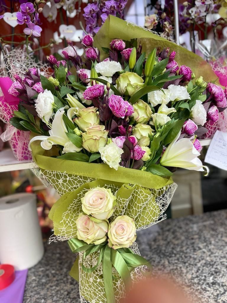 Bouquet di fiori rosa, bianchi e verdi avvolti in carta verde su un piano di lavoro in granito.