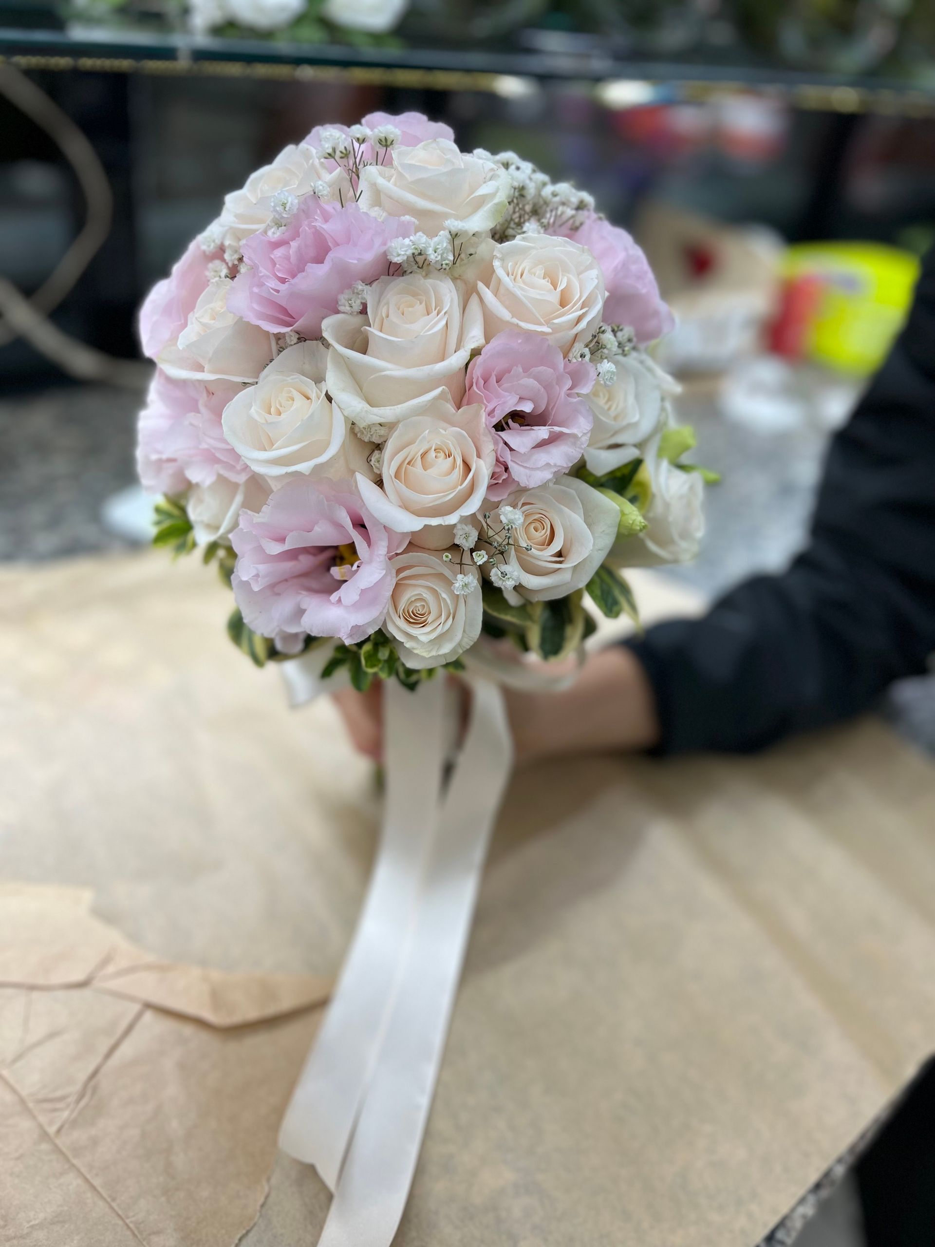 Piccolo mazzolino di rose color pastello con nastro bianco, tenuto in mano contro uno sfondo interno sfocato.