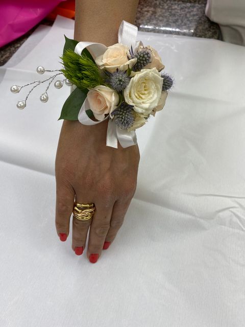 Mano con un corsage di rose bianche con nastro argentato e anello dorato su sfondo di stoffa bianca