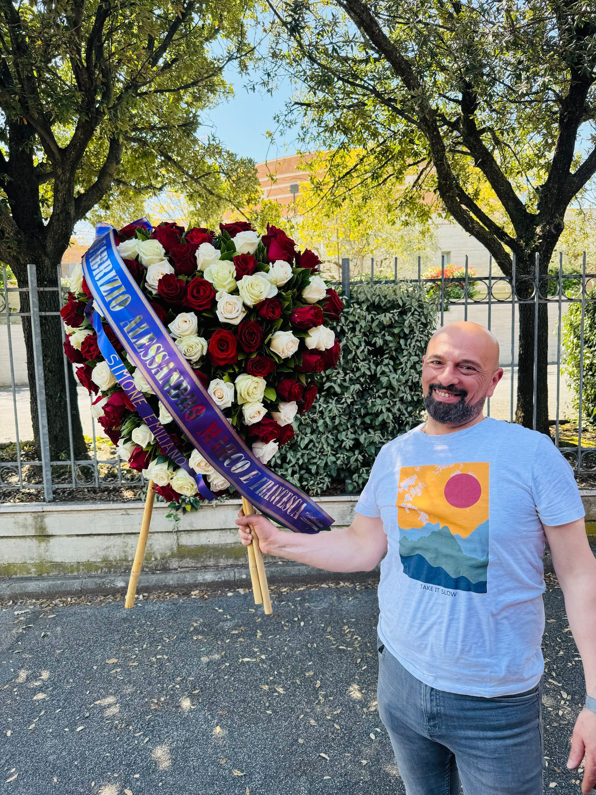 Un uomo in piedi all'aperto accanto a una grande ghirlanda di fiori rossi e bianchi con un nastro blu