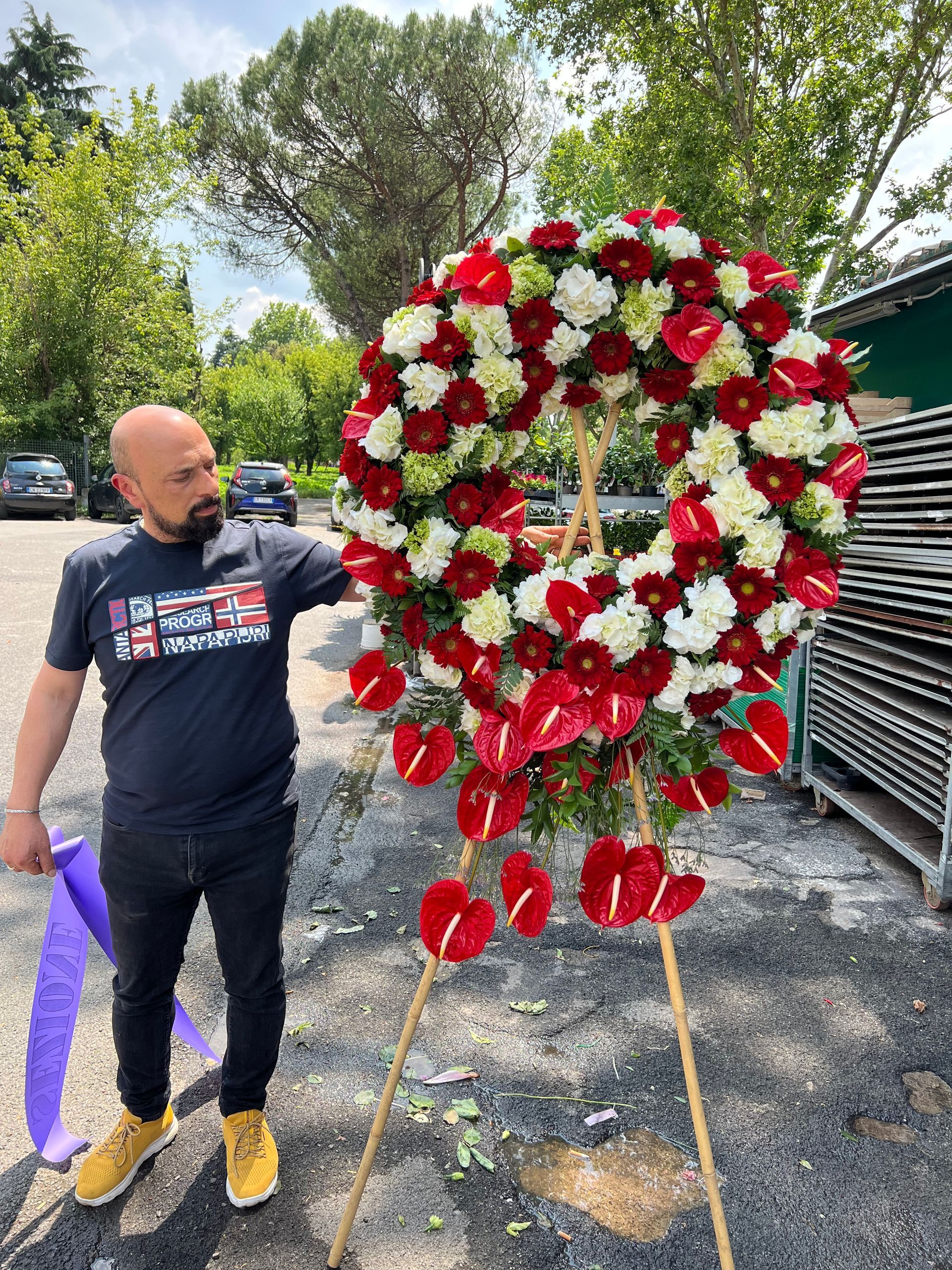 Un uomo in piedi accanto a una grande ghirlanda di fiori rossi e bianchi su un cavalletto all'aperto.