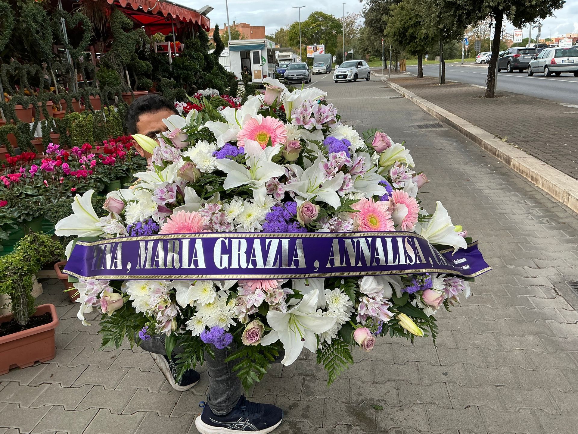 Grande corona funebre floreale con nastro viola su un marciapiede a lato di una strada