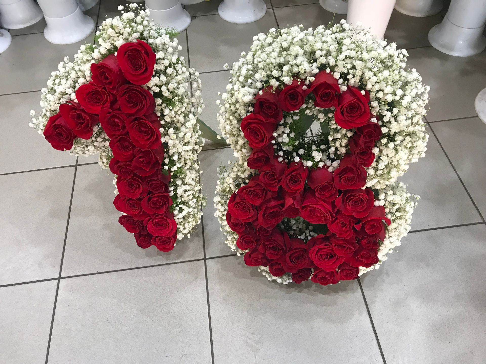 Composizione floreale a forma di numero 18 con rose rosse e fiori bianchi su un pavimento piastrellato