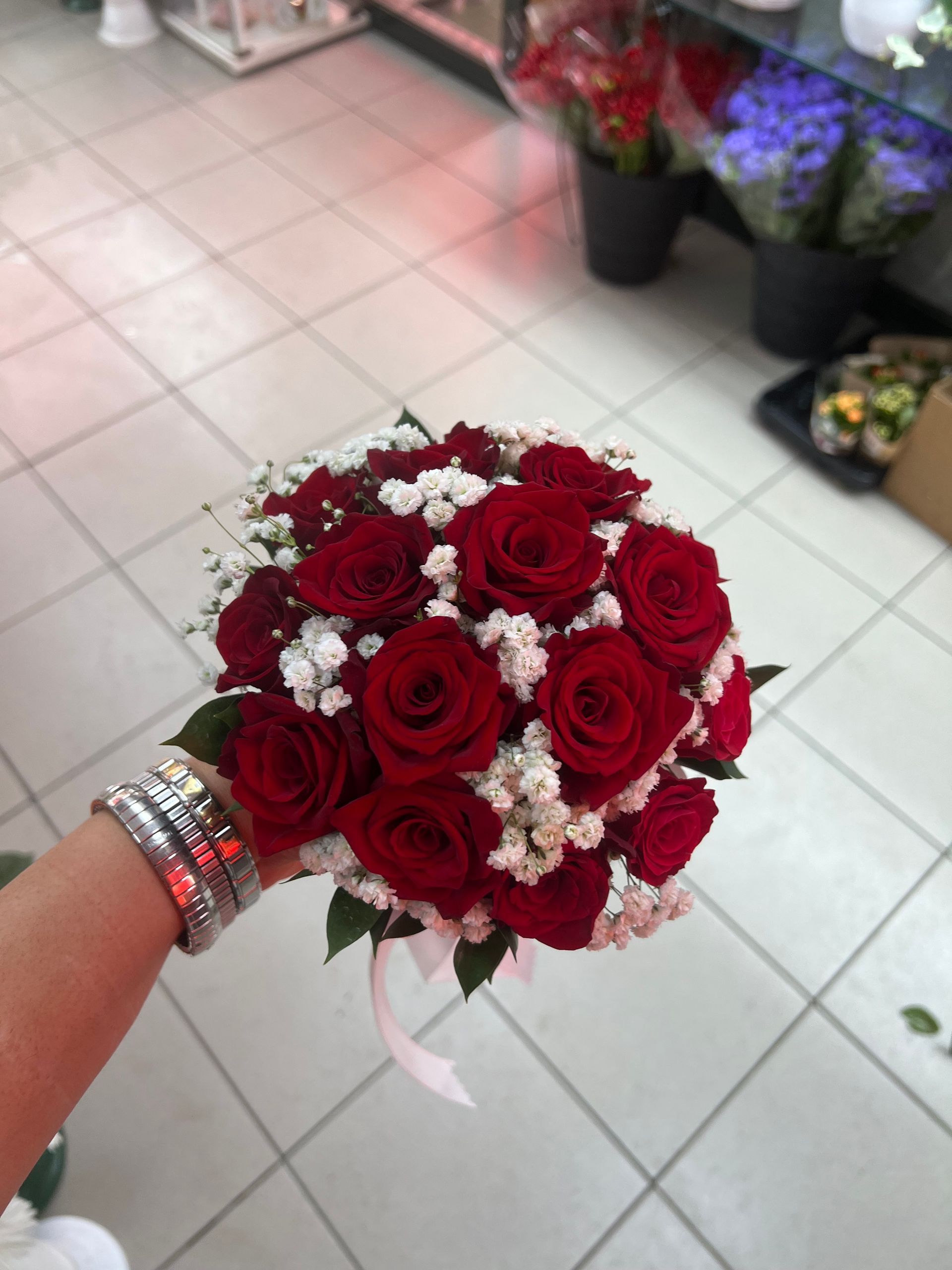 Bouquet di rose rosse con fiori di riempimento bianchi, tenuto in una mano decorata, in un ambiente interno.