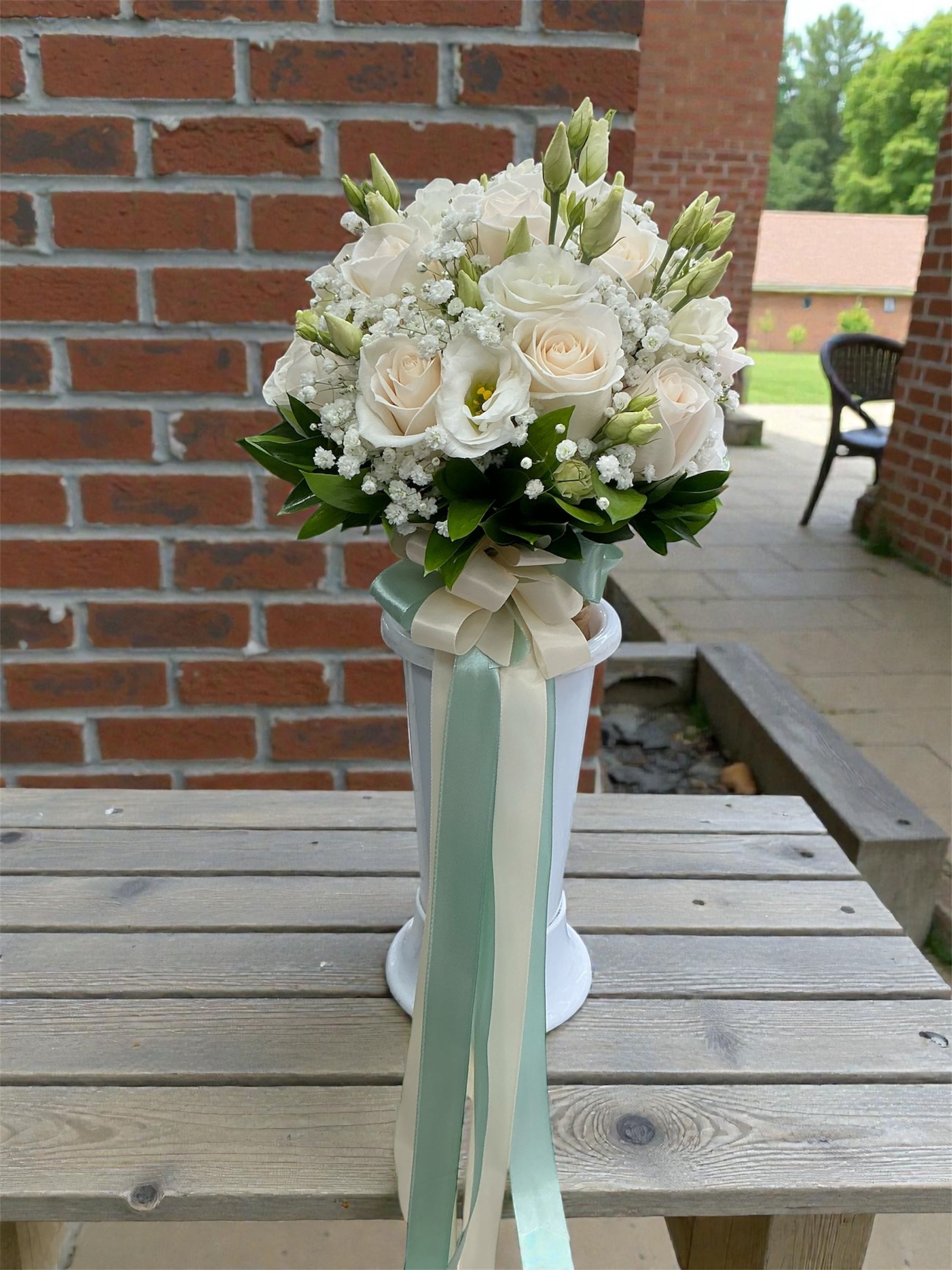 Bouquet di fiori bianchi con lunghi nastri in un vaso su un tavolo di legno all'aperto.