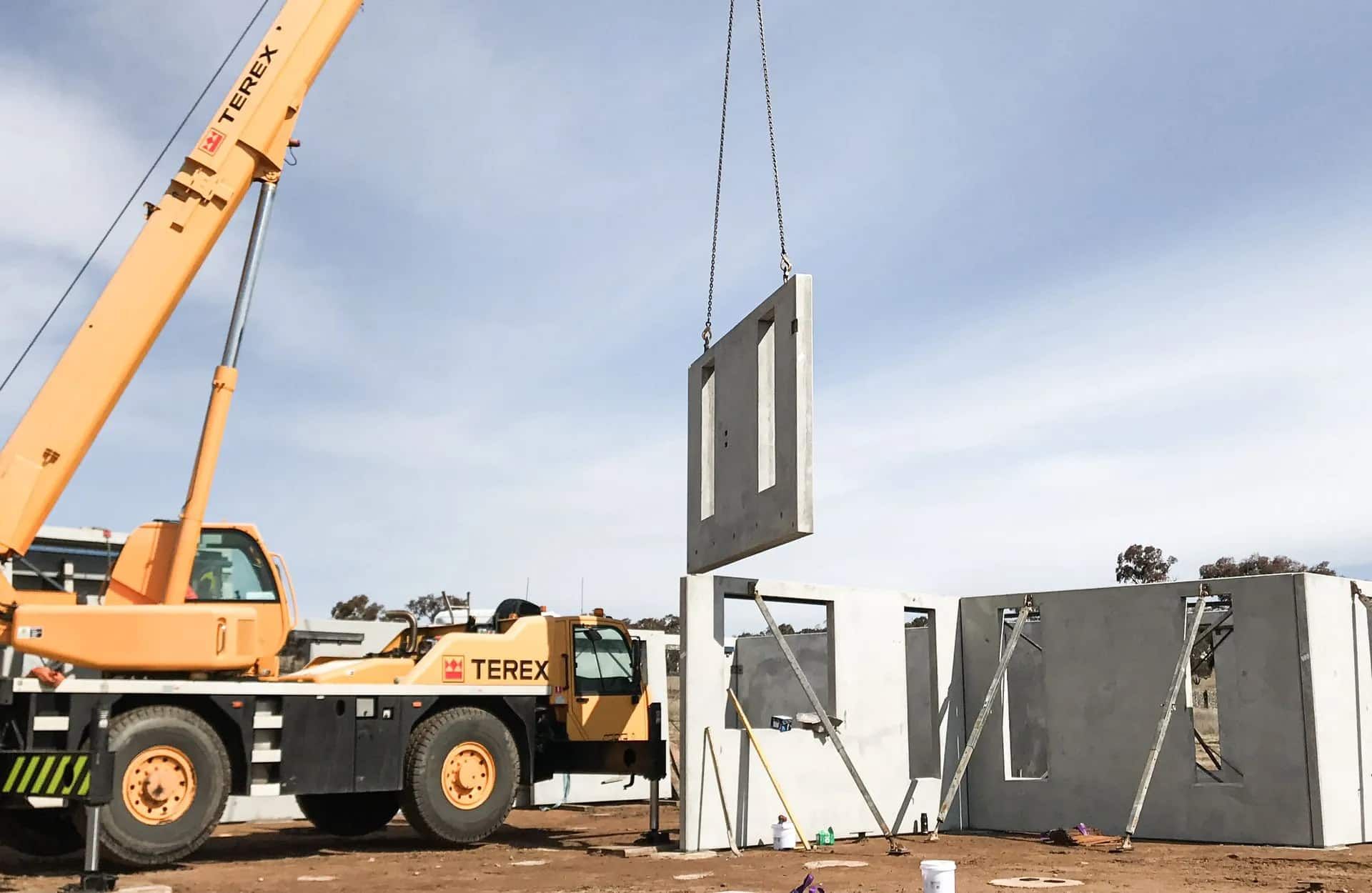 A Yellow Crane Lifting A Wall On A Dirt Field — Clearspan Builders In Queanbeyan East, NSW
