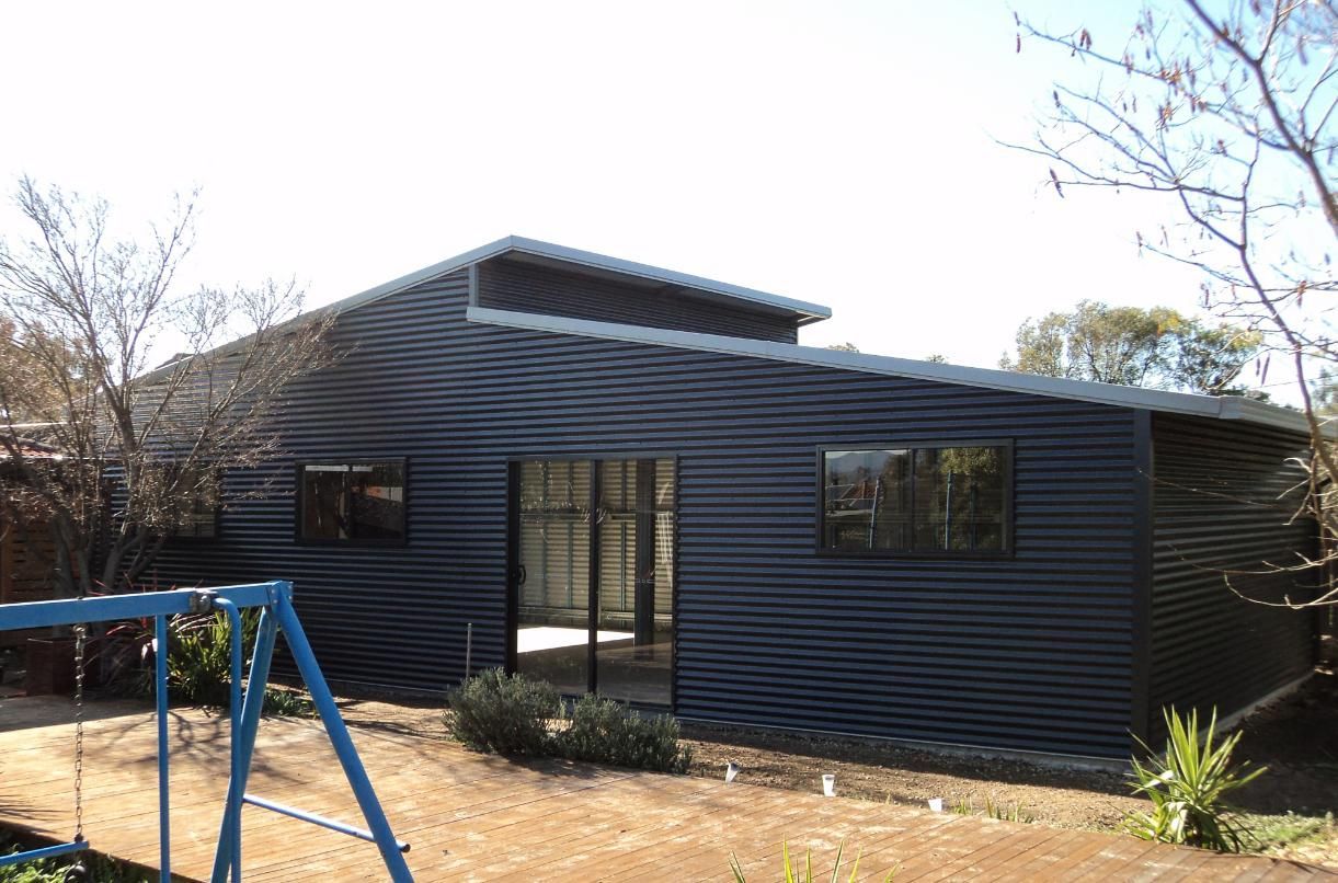A Black House with A Blue Swing Set in Front of It — Clearspan Builders In Queanbeyan East, NSW