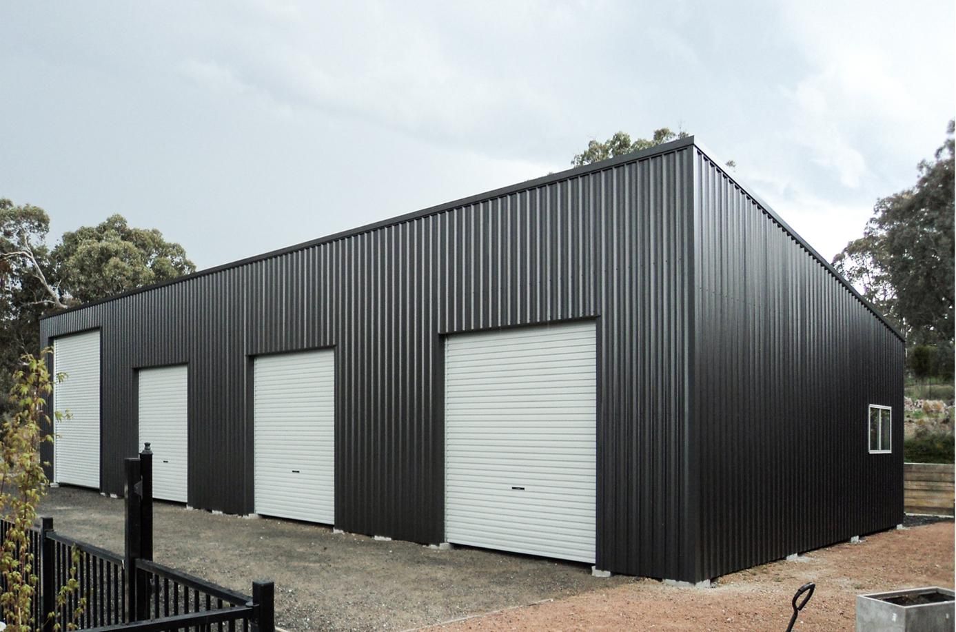A Large Black Building with White Garage Doors and A Fence in Front of It — Clearspan Builders In Queanbeyan East, NSW