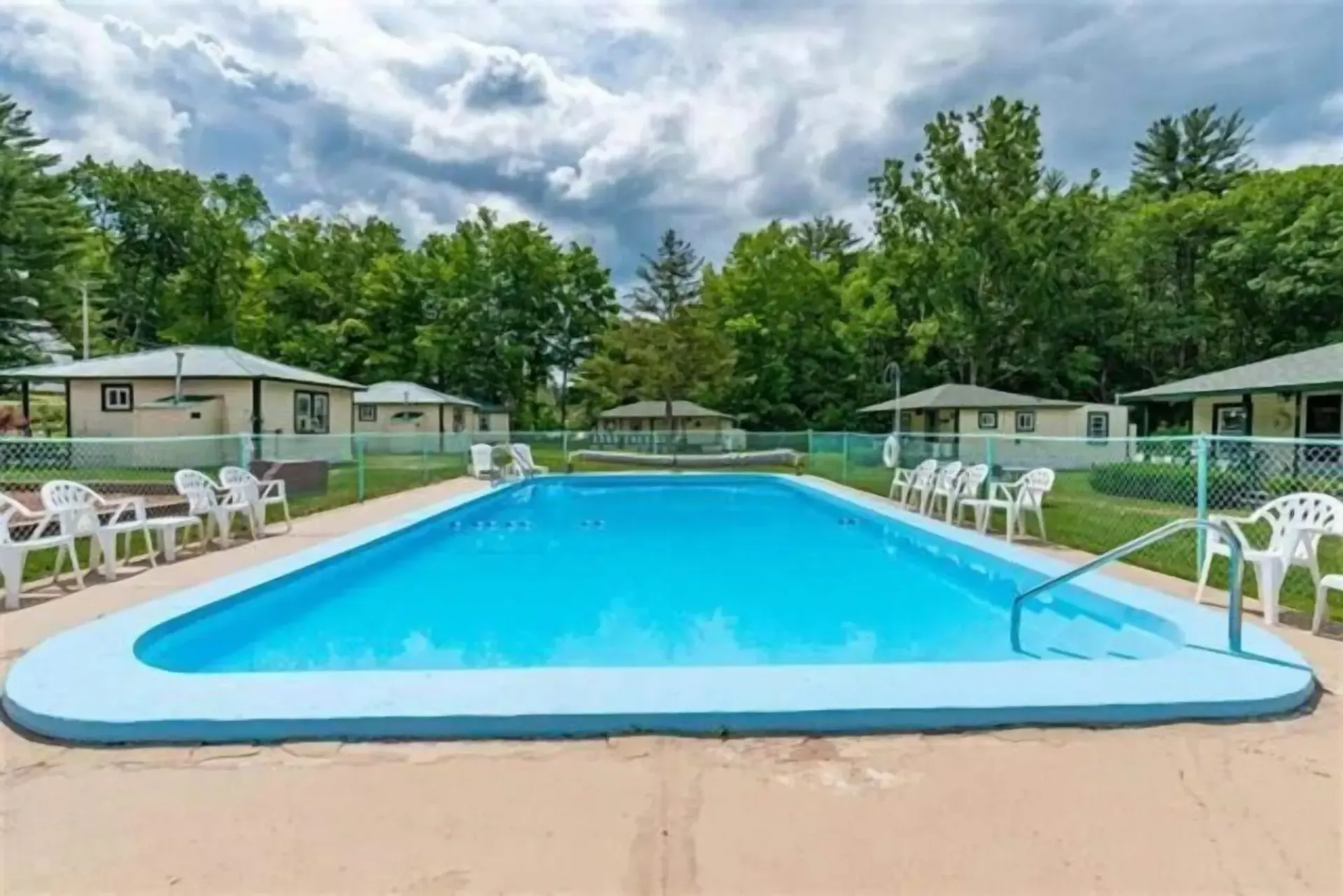 A large swimming pool is surrounded by chairs and houses.