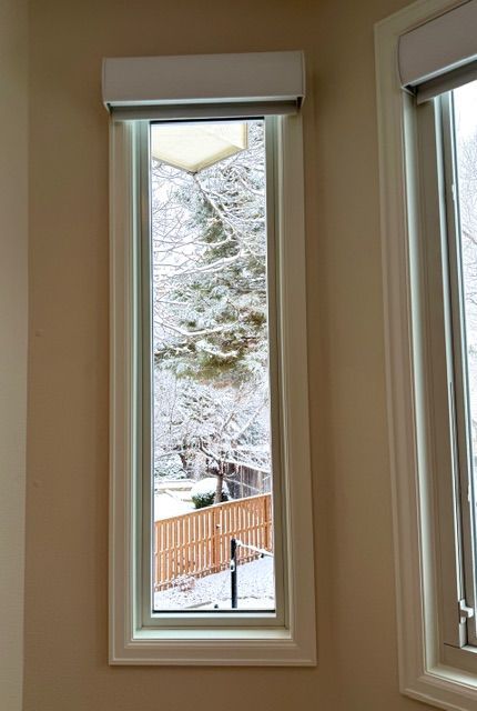 Tall, rectangular window showing a snowy scene outside. Light-colored window trim and shade, beige wall.
