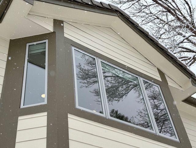 Close-up of a house exterior with large windows reflecting bare trees and snow falling.