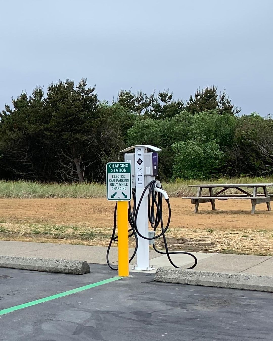Electric vehicle charging station in parking lot, sign reads 'Charging Station Electric Vehicles Only While Charging.'