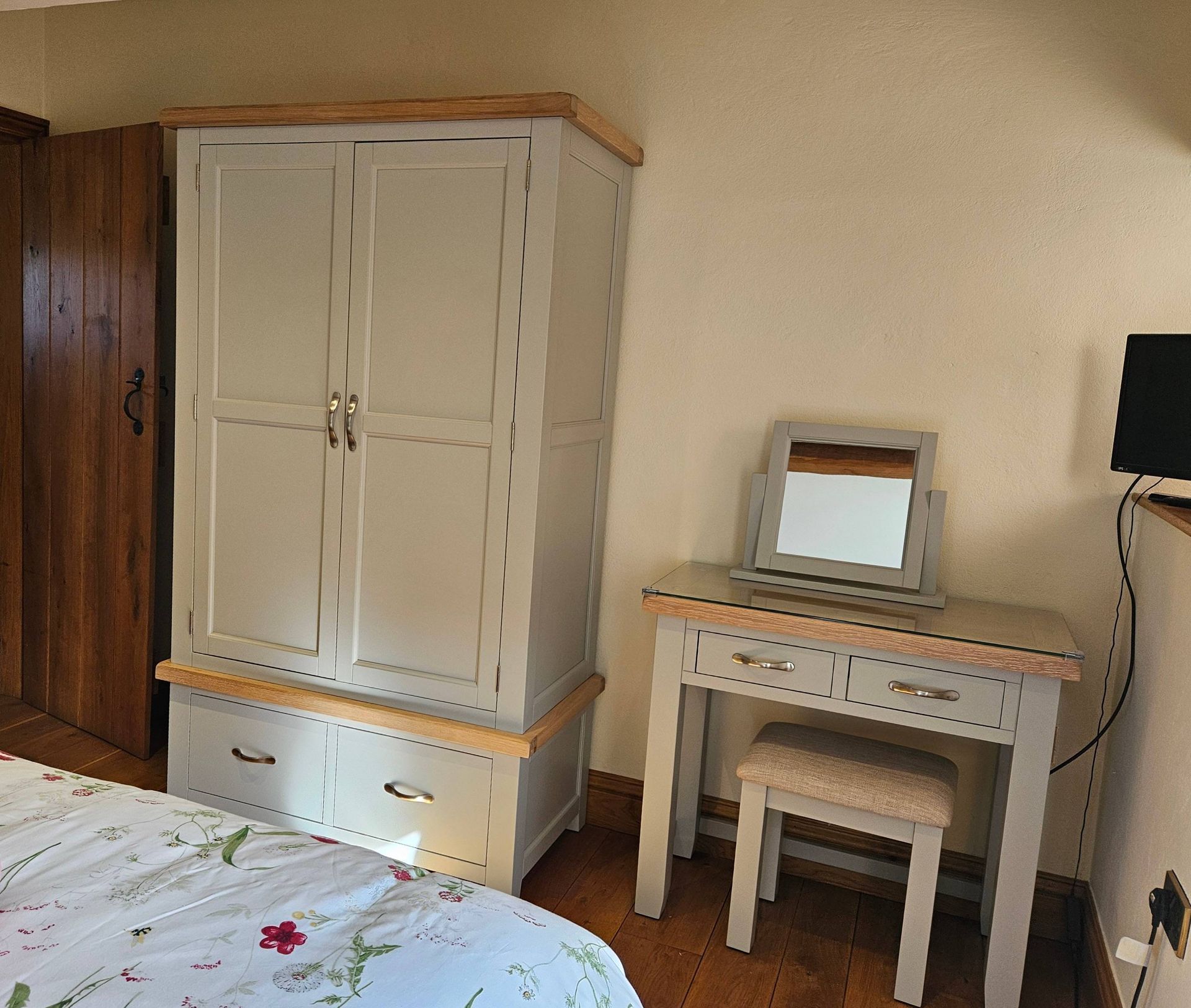 Bedroom with gray wardrobe, vanity, and wooden door. A floral bedspread is visible.