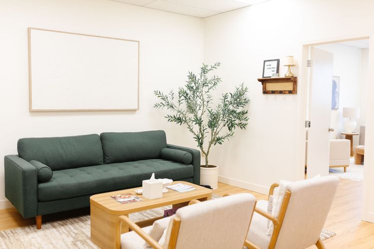 Bright living room with beige sofas, round wooden coffee table, and large window with trees outside