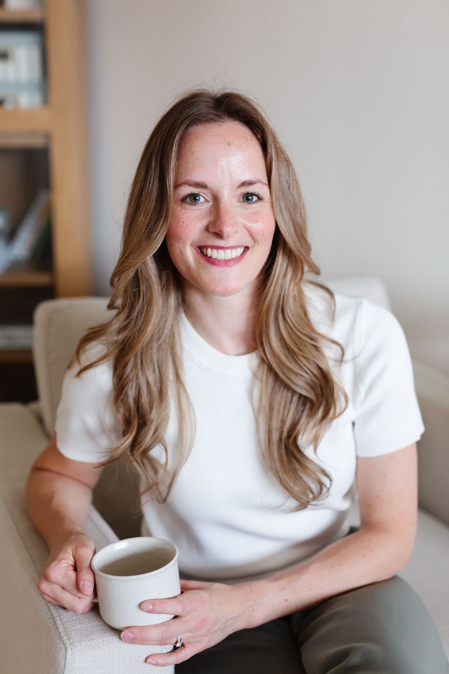 Smiling woman in a white shirt holding a mug while seated indoors on a couch